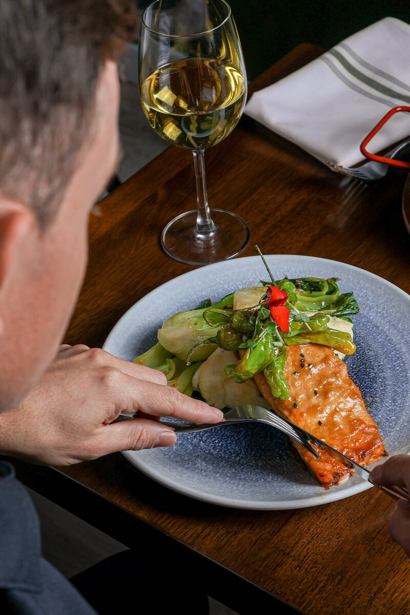 Guest eating salmon entree with glass of white wine