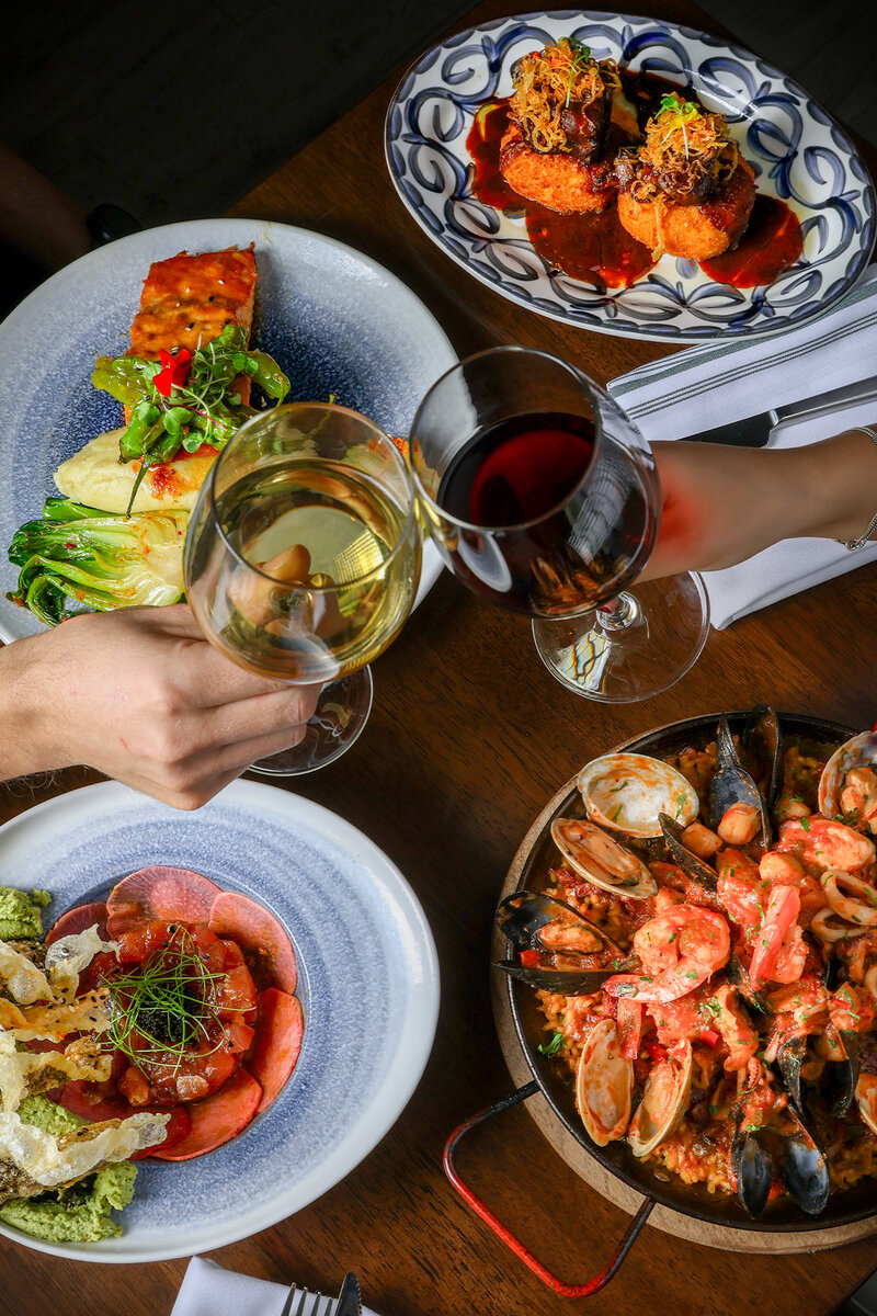 Two guests cheering with wine glasses with set table with multiple entrees